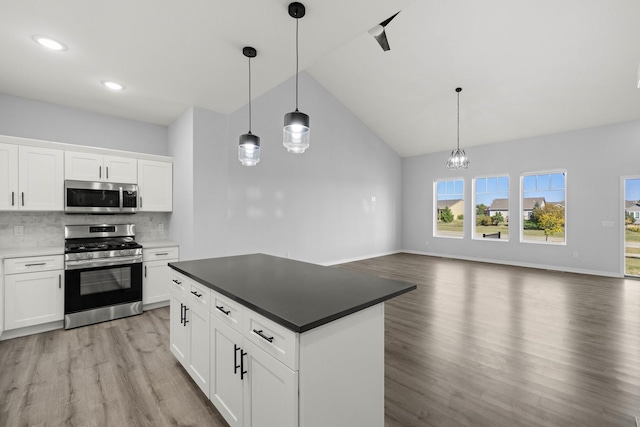 kitchen featuring appliances with stainless steel finishes, tasteful backsplash, white cabinets, decorative light fixtures, and light hardwood / wood-style flooring