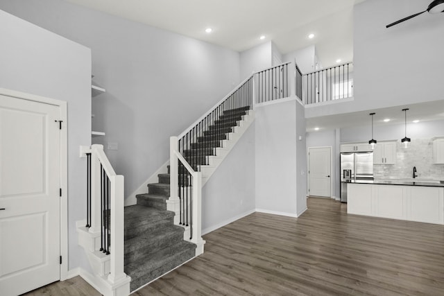 stairs with ceiling fan, a high ceiling, hardwood / wood-style floors, and sink