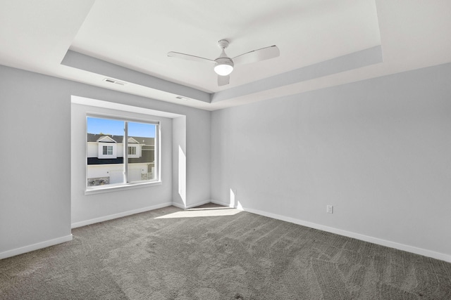 spare room with ceiling fan, a raised ceiling, and carpet flooring