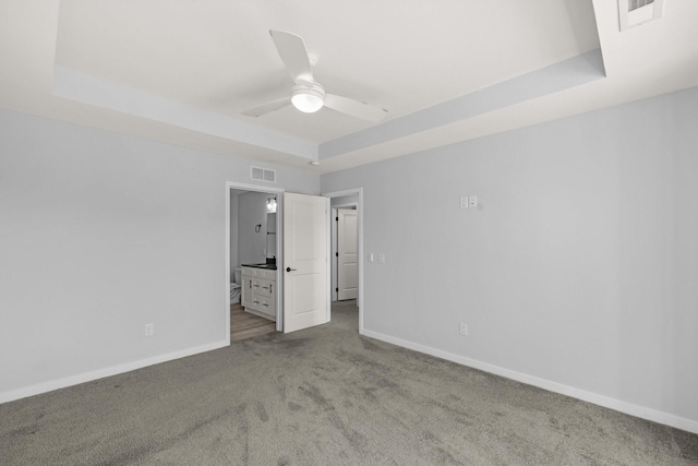 unfurnished bedroom with ceiling fan, connected bathroom, and a tray ceiling