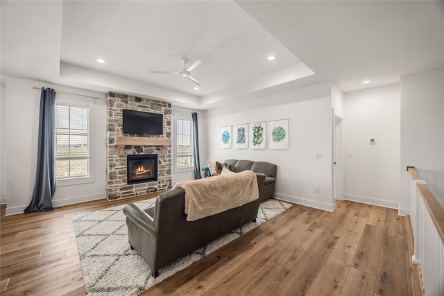 living room featuring ceiling fan, a raised ceiling, light hardwood / wood-style floors, and a fireplace