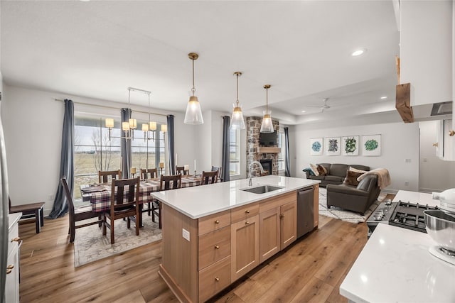 kitchen featuring light brown cabinets, sink, hanging light fixtures, a kitchen island with sink, and stainless steel dishwasher