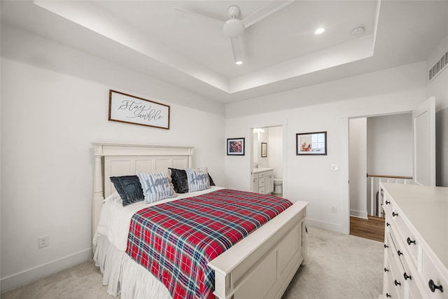 carpeted bedroom featuring ceiling fan, a raised ceiling, and ensuite bath