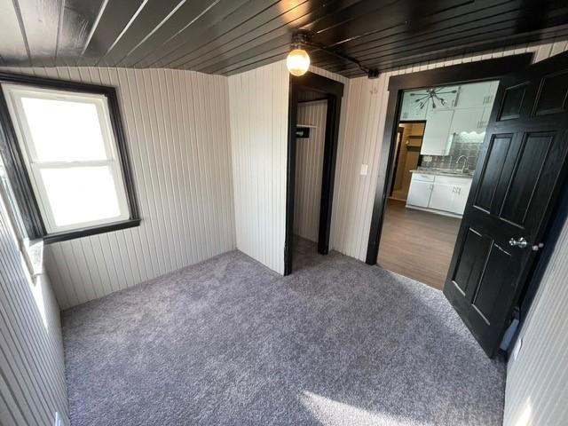 unfurnished bedroom with dark carpet, sink, and wood walls