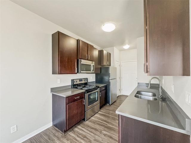 kitchen with sink, stainless steel appliances, dark brown cabinets, and light hardwood / wood-style floors