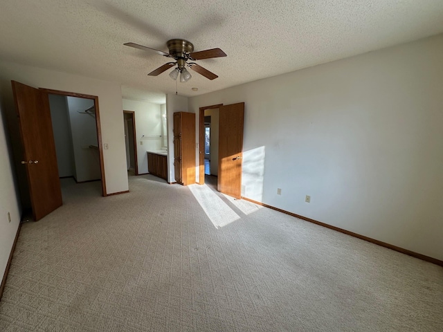 unfurnished bedroom with ensuite bathroom, a spacious closet, a textured ceiling, light carpet, and ceiling fan