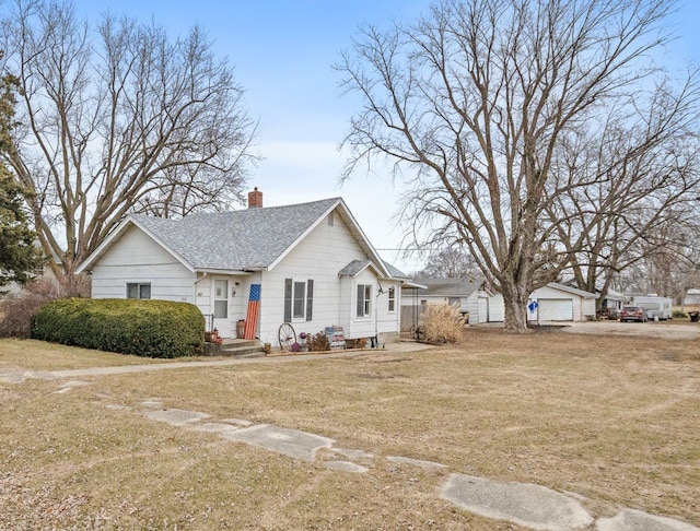 view of front of property featuring a garage, a front yard, and an outbuilding