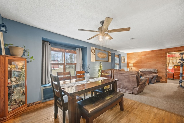 dining room with ceiling fan, a textured ceiling, light wood-type flooring, and wooden walls