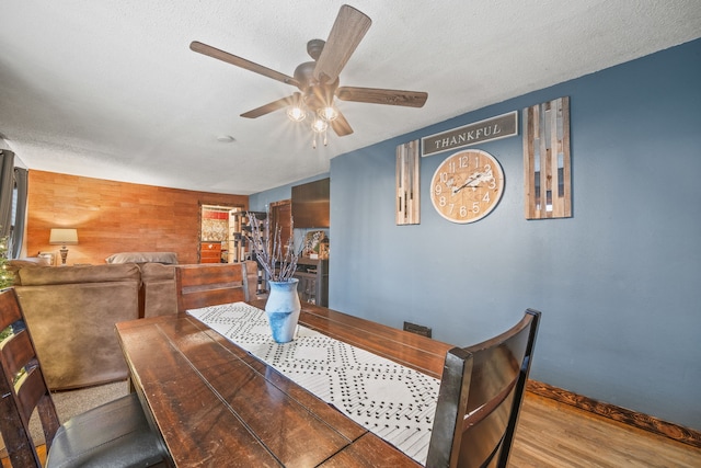 dining room with light hardwood / wood-style floors, a textured ceiling, wood walls, and ceiling fan