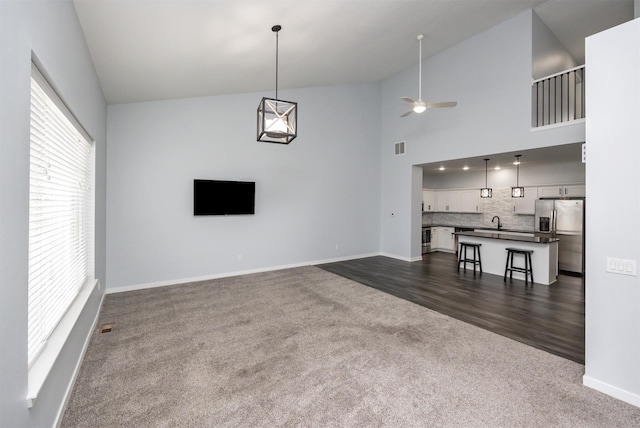 unfurnished living room featuring sink, ceiling fan, dark carpet, and high vaulted ceiling