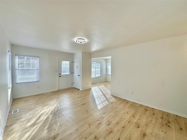 unfurnished room with light hardwood / wood-style floors, a wealth of natural light, and a textured ceiling