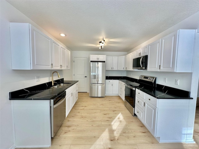 kitchen featuring a textured ceiling, white cabinetry, sink, light wood-type flooring, and stainless steel appliances