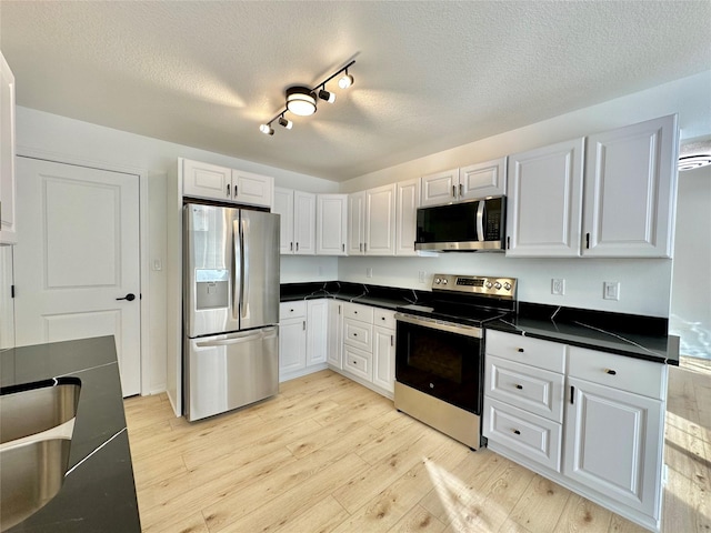 kitchen featuring appliances with stainless steel finishes, a textured ceiling, white cabinetry, track lighting, and light hardwood / wood-style flooring