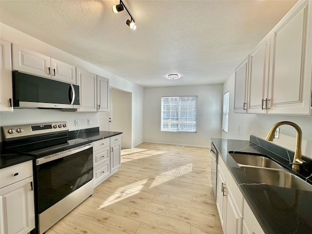 kitchen with white cabinets, a textured ceiling, appliances with stainless steel finishes, and light wood-type flooring