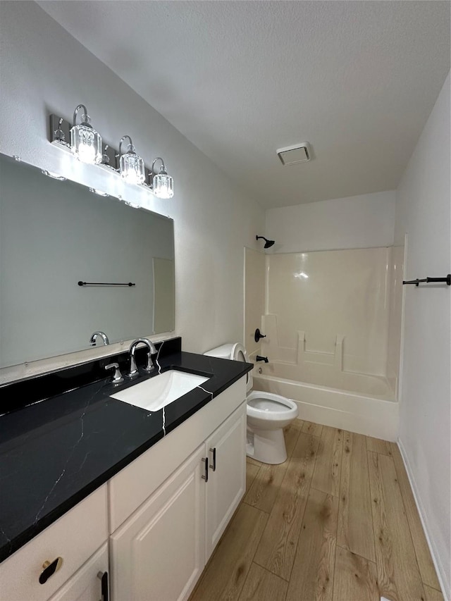 full bathroom with wood-type flooring, toilet, a textured ceiling, vanity, and washtub / shower combination