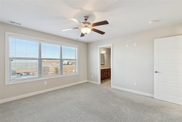 unfurnished bedroom featuring a textured ceiling, light colored carpet, ensuite bath, visible vents, and baseboards
