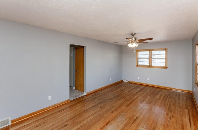 spare room featuring light wood-type flooring, ceiling fan, and a textured ceiling