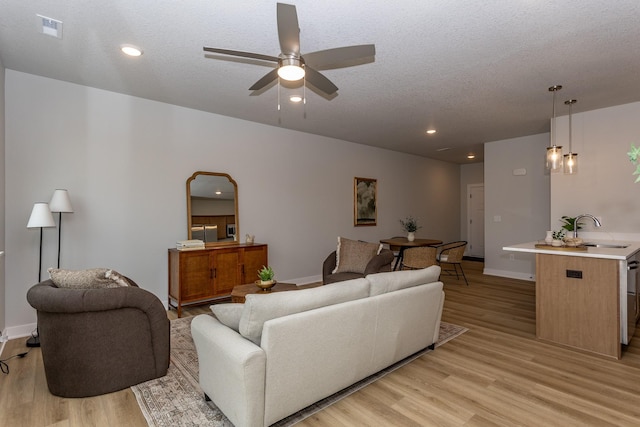 living room featuring a textured ceiling, ceiling fan, and light wood finished floors