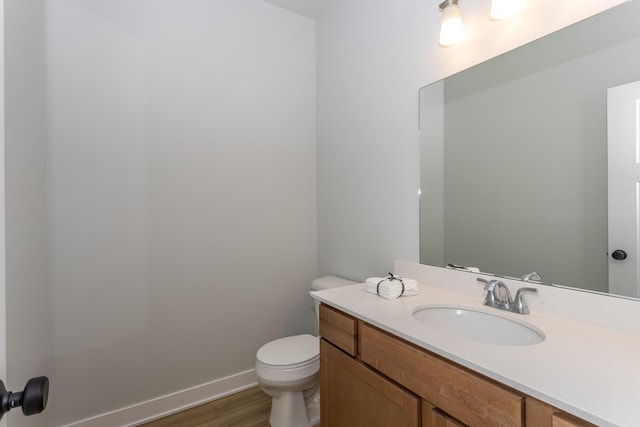 half bath featuring baseboards, vanity, toilet, and wood finished floors