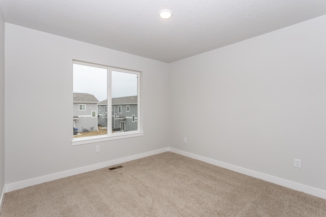 empty room with a textured ceiling, carpet, visible vents, and baseboards