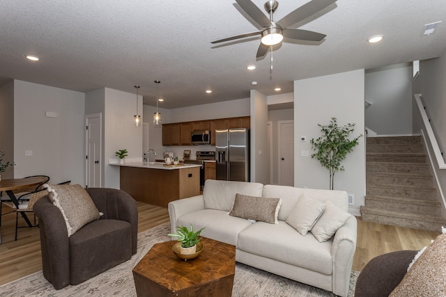 living area with ceiling fan, stairway, a textured ceiling, light wood-type flooring, and recessed lighting