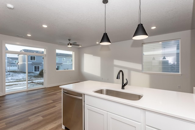 kitchen featuring sink, dishwasher, white cabinetry, hanging light fixtures, and a textured ceiling