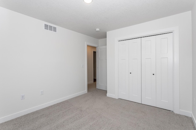 unfurnished bedroom with light colored carpet, a closet, and a textured ceiling