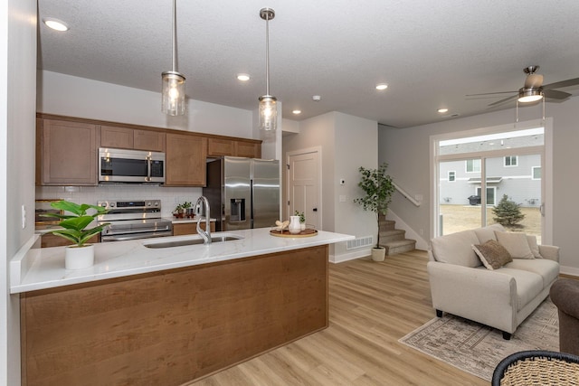 kitchen featuring hanging light fixtures, brown cabinetry, stainless steel appliances, and a sink