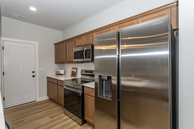 kitchen with appliances with stainless steel finishes, brown cabinets, light countertops, and visible vents