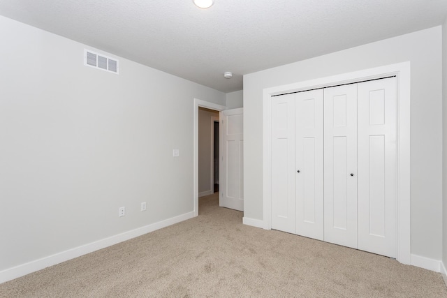 unfurnished bedroom featuring baseboards, visible vents, a textured ceiling, and light colored carpet