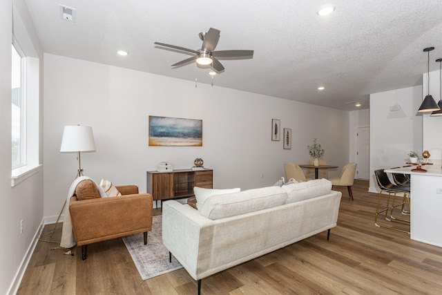 living room with a textured ceiling, light hardwood / wood-style floors, and ceiling fan