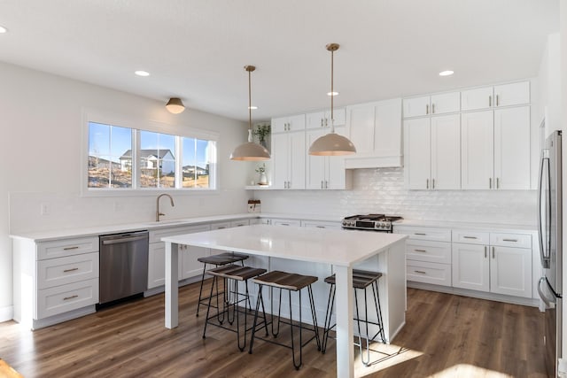 kitchen with pendant lighting, appliances with stainless steel finishes, a kitchen breakfast bar, white cabinets, and a kitchen island