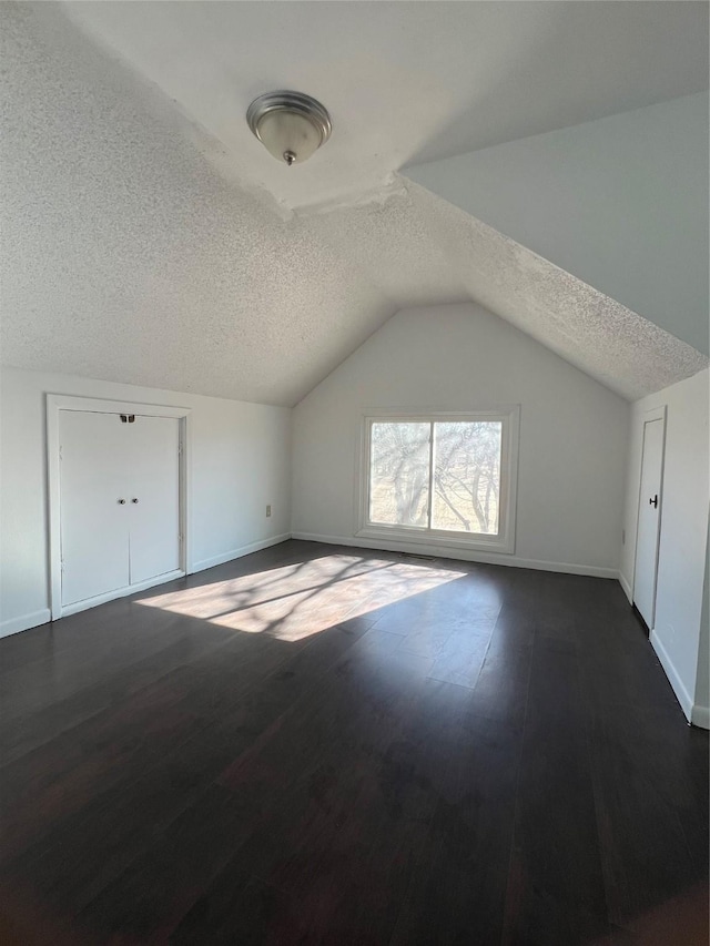 additional living space with vaulted ceiling, dark wood-type flooring, and a textured ceiling