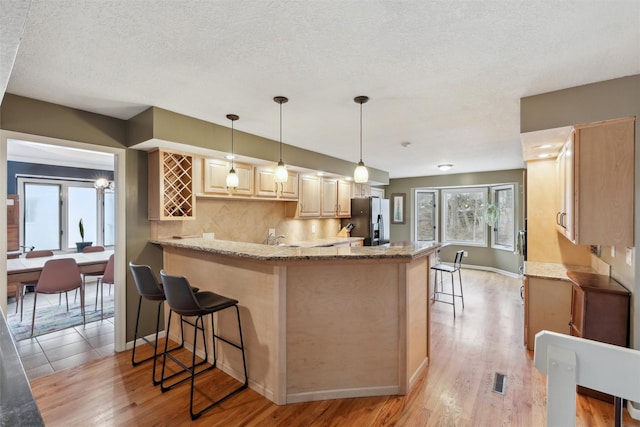 kitchen with a peninsula, light stone countertops, stainless steel fridge, and light brown cabinetry