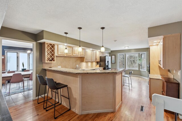 kitchen featuring light brown cabinetry, stainless steel fridge, a peninsula, and light stone counters