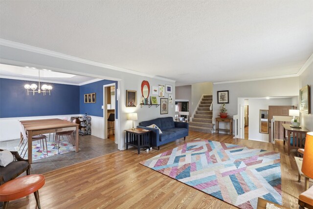 living area with a textured ceiling, wood finished floors, stairway, an inviting chandelier, and crown molding