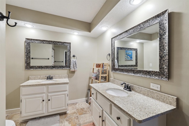 bathroom featuring two vanities, baseboards, and a sink