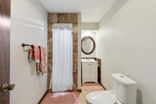 bathroom with baseboards, toilet, vanity, and a tile shower