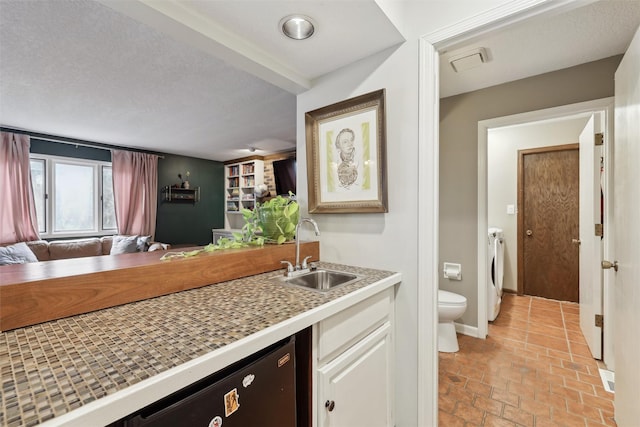 kitchen featuring a sink, washing machine and dryer, open floor plan, white cabinets, and light countertops