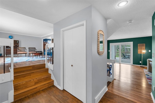 hall featuring baseboards, wood finished floors, visible vents, and a textured ceiling