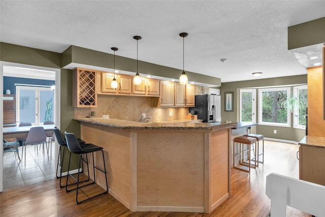 kitchen featuring light wood finished floors, a breakfast bar, fridge with ice dispenser, decorative backsplash, and a textured ceiling