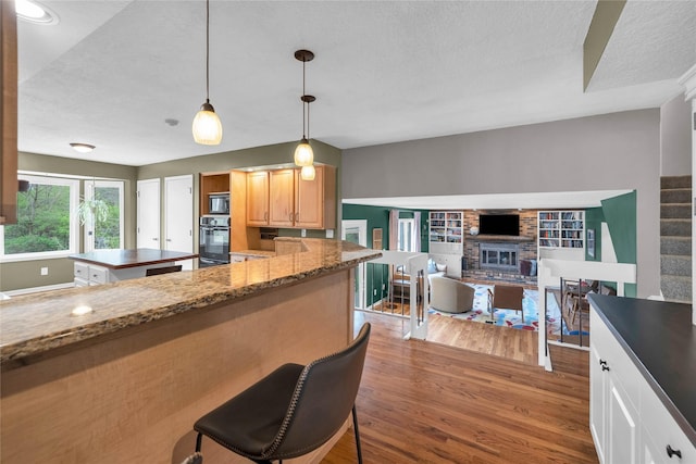 kitchen featuring black appliances, wood finished floors, a textured ceiling, and a fireplace