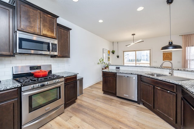 kitchen with stainless steel appliances, backsplash, a sink, dark brown cabinetry, and light wood-type flooring