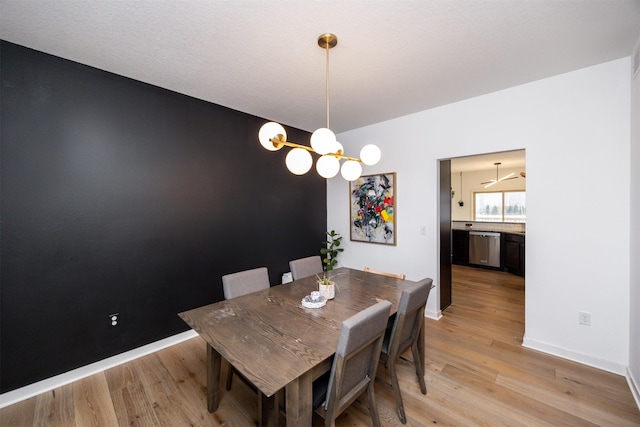 dining room featuring baseboards, an accent wall, a chandelier, and light wood-style floors