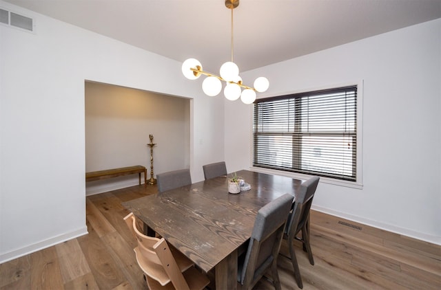 dining space featuring baseboards, visible vents, an inviting chandelier, and wood finished floors