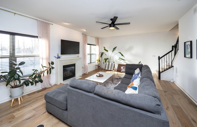 living room featuring ceiling fan, a fireplace with flush hearth, wood finished floors, baseboards, and stairway