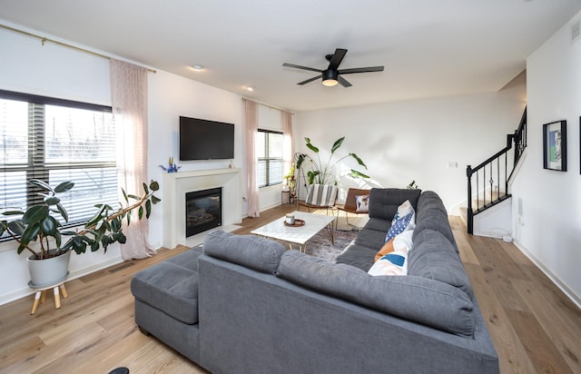 living area featuring a fireplace with flush hearth, a ceiling fan, wood finished floors, and stairway
