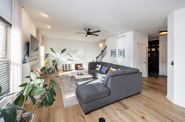 living room featuring stairway, ceiling fan, light wood-style flooring, baseboards, and visible vents