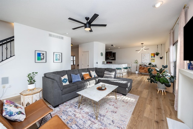 living room featuring a ceiling fan, visible vents, stairway, and light wood-style flooring