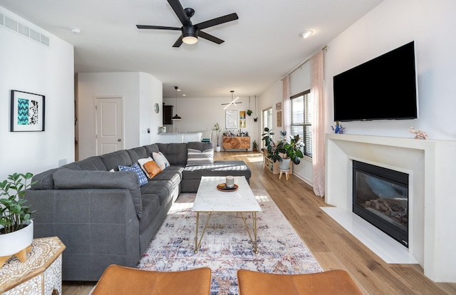 living room with a glass covered fireplace, a ceiling fan, visible vents, and light wood-style floors